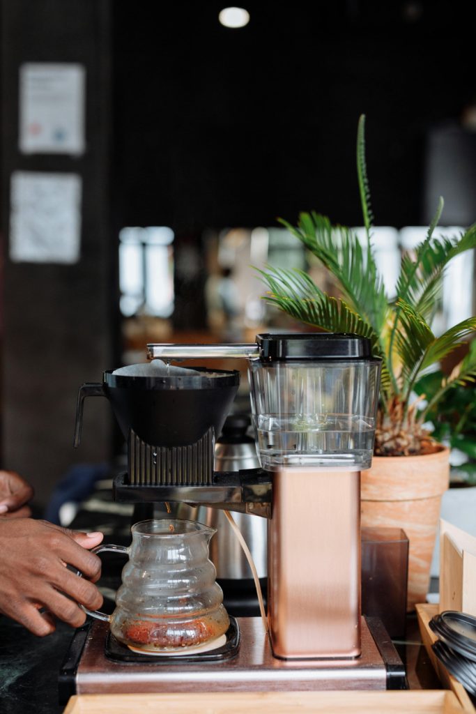 Kaffee läuft in eine Glaskaraffe in einer Filterkaffeemaschine. Die Glaskaraffe wird von einer Hand gehalten.